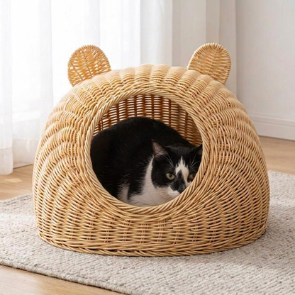 Chat noir et blanc installé dans un panier en rotin pour chat avec ouverture ronde et oreilles tressées