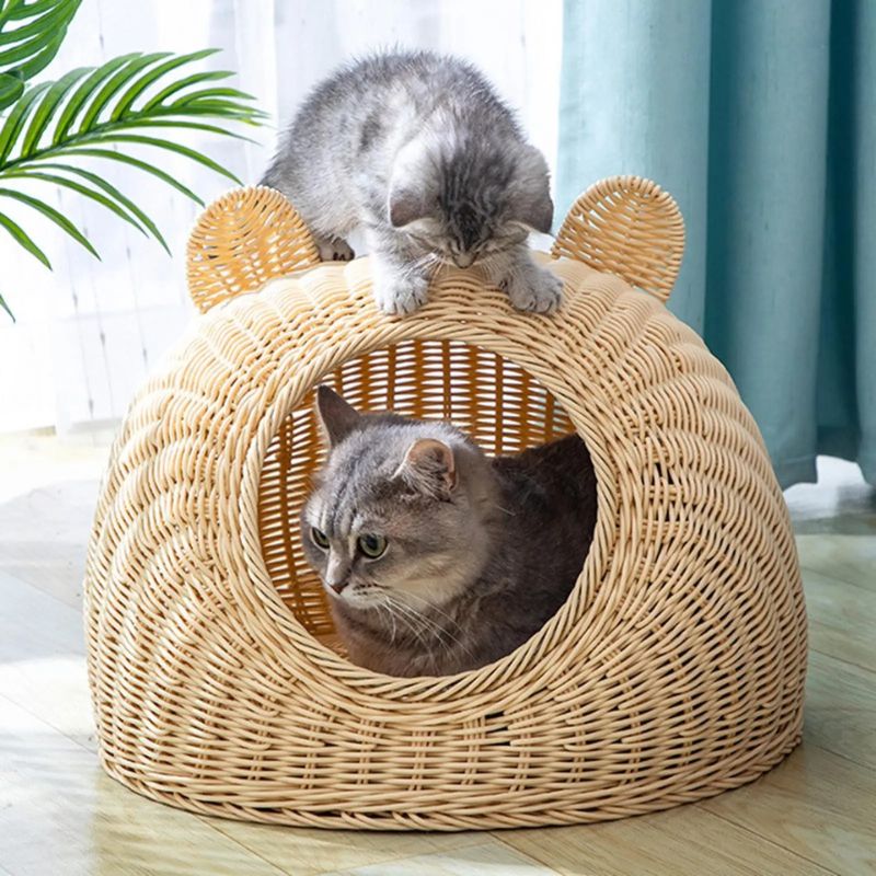 Panier en rotin pour chat avec ouverture ronde et oreilles tressées, un chat à l’intérieur et un autre penché sur le dessus 