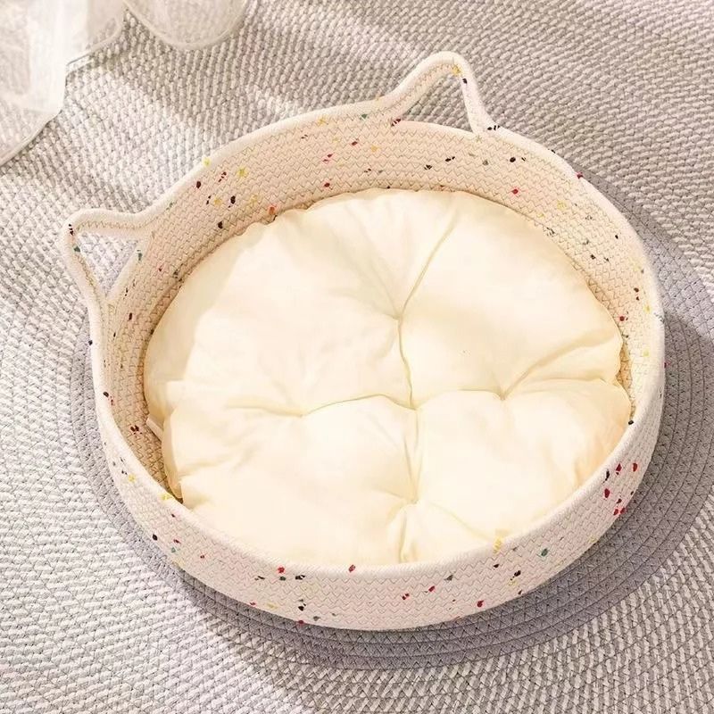 Panier pour chat en rotin à deux poignées avec coussin blanc, posé sur un tapis gris