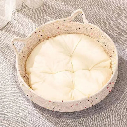 Panier pour chat en rotin à deux poignées avec coussin blanc, posé sur un tapis gris