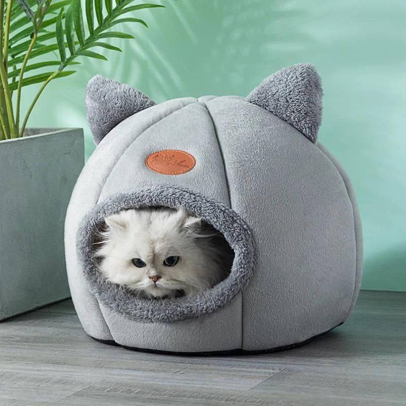 Panier pour chat grotte gris avec un chat blanc à l’intérieur.